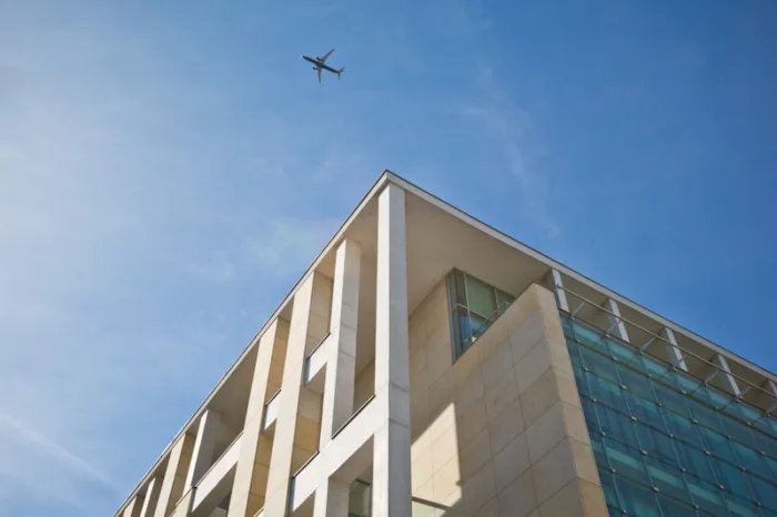 Budynek Centrum Edukacyjnego Usług Elektronicznych z dolnej perspektywy, na niebie widnieje lecący samolot.