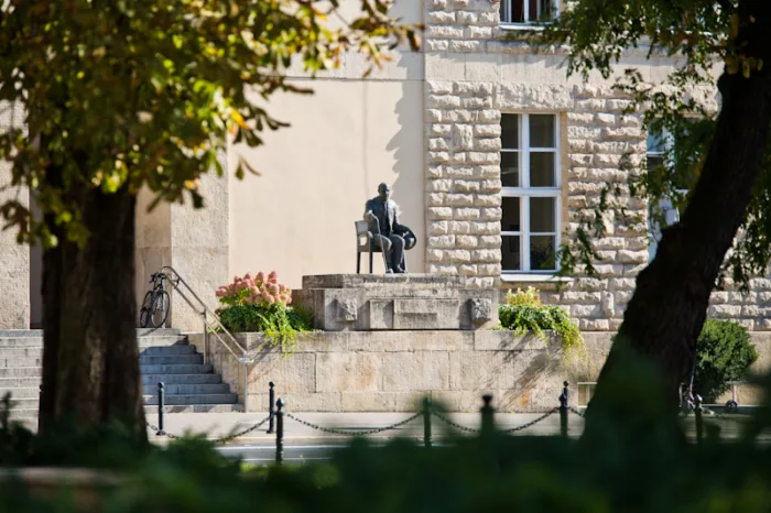 Pomnik siedzącego na krześle Zbigniewa Zakrzewskiego przed Budynkiem A Uniwersytetu Ekonomicznego w Poznaniu. W prawej ręce trzyma laskę, a w prawej kapelusz.