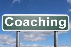 Znak drogowy z napisem Coaching na tle nieba z chmurami.