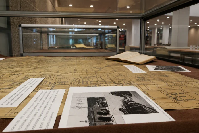 Eksponaty w szklanej gablocie wystawowej, m.in. rozłożona historyczna mapa, archiwalna fotografia i otwarta książka.