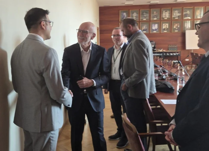 Mężczyźni w garniturach witają się i rozmawiają w sali konferencyjnej przed rozpoczęciem spotkania.